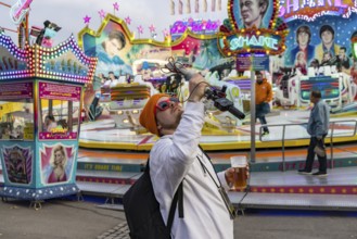 Influencer with live camera and beer in front of a fairground ride. Cannstatter Volksfest at the