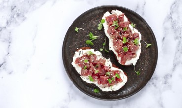 Sandwiches, rye bread with cream cheese, sliced tuna fillet with herbs, breakfast on a black plate,
