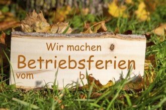Company holidays autumn: Wooden sign with added text WIR MACHEN BETRIEBSFERIEN VOM/BIS in a meadow
