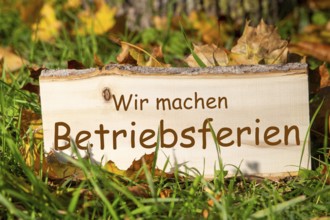 Company holidays autumn: Wooden sign with added text WIR MACHEN BETRIEBSFERIEN in a meadow with