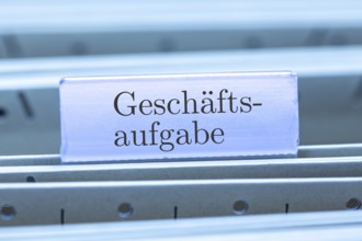 (Photomontage) Sign with the inscription GESCHÄFTSAUFGABE on a suspension file index