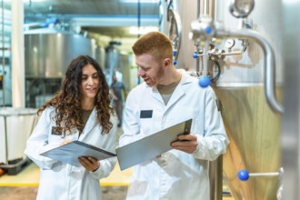 Two brewery workers in lab coats inspecting machinery and documenting processes, ensuring product