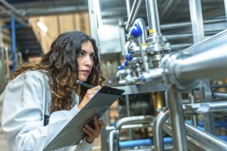 Woman in a white coat diligently checking and documenting the status of stainless steel pipes and