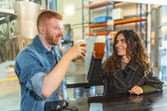 Young man and woman clinking craft beer glasses and smiling at a modern microbrewery bar, enjoying