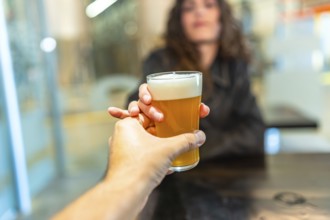 Hand holding a refreshing glass of craft beer, presenting it to a woman in a bar, representing