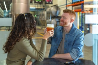 Young couple on a brewery date tasting craft beer, smiling and relaxed in a modern industrial