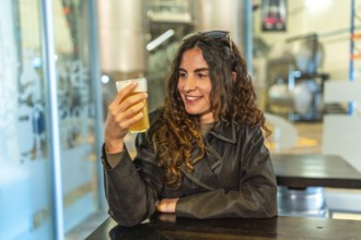 Woman in a leather jacket smiling and savoring a glass of craft beer at a modern brewery bar,