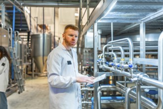 Young male specialist wearing a white lab coat and observing pipes and machinery while holding a