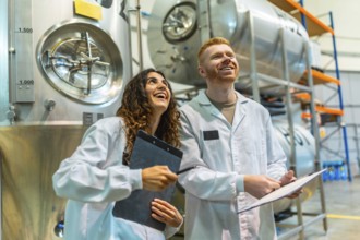 Smiling man and woman in lab coats holding clipboards, overseeing production and quality control in