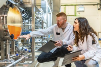 Two professional brewery workers wearing lab coats examining the liquid level inside a stainless
