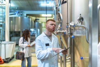 Brewery quality control team inspecting industrial fermentation tanks, a technician monitoring data