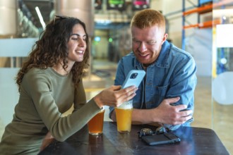 Young couple sitting at a table in a brewery or beer factory, having a conversation and sharing