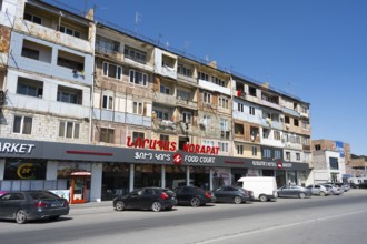 A multi-storey residential building with shops on the ground floor on a busy street, Norapat,