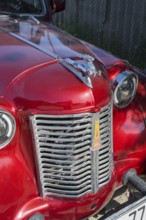 Front of a shiny red vintage car with a striking emblem in the sun, Moskvich 401, Armavir province,