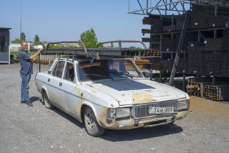A rusty old car with a man putting metal rods on it, middle class car GAZ-24 Volga, Norapat,