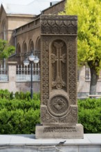 A detailed khachkar with a cross motif and rich ornamentation in front of a church façade,