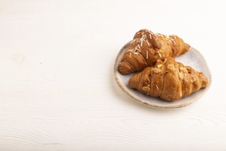 Croissant on blue plate on white wooden background, side view, copy space