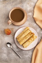Waffles with caramel on brown concrete background and orange linen textile, cup of coffee, top