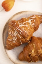 Croissant on blue plate on white wooden background and orange linen textile, cup of coffee, side