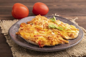 Baked chicken meat with cheese and tomatoes on brown wooden background and linen textile. side