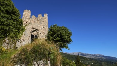 Ancient ruined tower with neighbouring trees against a picturesque blue sky and mountain backdrop,