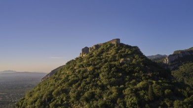 Byzantine castle from the 13th century AD on a green hill in the sunrise, surrounded by forest,