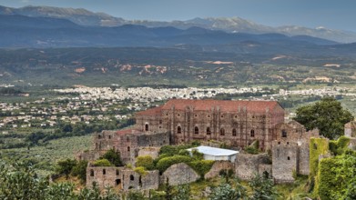 Byzantine palace of Mystras rises above a green landscape with mountains in the background,