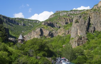 A picturesque gorge with steep rock faces and lush greenery, a church in the background, blue sky