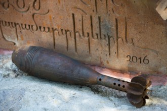Rusty grenade lies in front of an engraved memorial plaque with the year 2016, mortar shell,