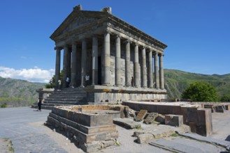 Ancient temple with columns in front of a mountainous landscape under a clear sky, Greek-Roman
