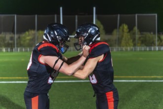 Two american football players in black and orange uniforms collide in a gritty close up on green