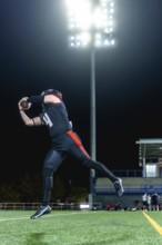 American football player in black and orange uniform catching an airborne football on a green turf