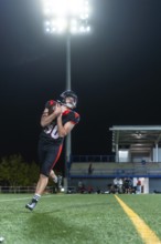 American football player in uniform and helmet catching the football on a green turf field at night