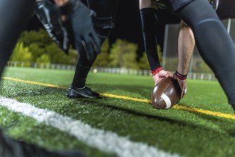 American football player is positioning the leather ball on the marked artificial turf field during