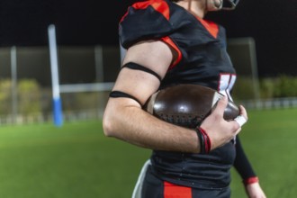 American football player preparing for a game, holding a ball firmly on a sports field lit by