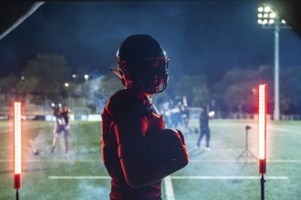 American football player in full gear holding a ball, standing confidently on a floodlit stadium
