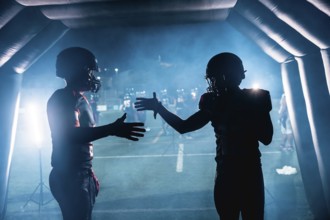 American football players in silhouettes high fiving each other inside a smoky stadium tunnel at