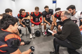 American football coach kneeling, explaining game strategy to a team of young athletes in full