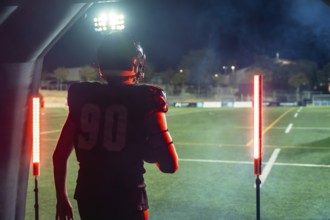 American football player in full uniform and helmet emerging from a tunnel onto a floodlit stadium