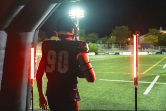 American football player wearing helmet and uniform with number 90, holding a football, walking