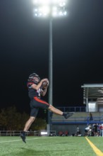American football player in uniform and helmet leaping to catch the ball mid air on a floodlit