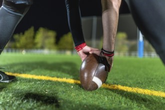 Football player positioning brown leather ball on yellow line on green grass, hands steadying ball