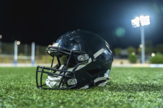 American football helmet lying on green artificial turf field with goal posts and bright stadium