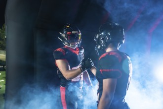 American football players wearing uniforms and helmets shaking hands, showing sportsmanship and