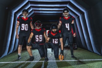 American football players in black and red uniforms, some kneeling and some standing in a dark