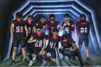 American football team players in uniforms and helmets posing together inside a stadium inflatable