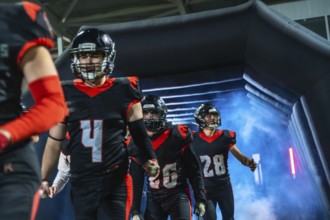 American football players, wearing black and red uniforms with helmets, walking into the stadium
