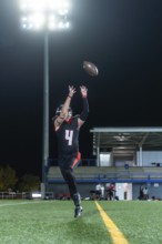 American football athlete in uniform and helmet jumping during a night game on a stadium field,