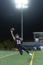American football player in uniform and helmet is mid air, making a dynamic catch of a pigskin ball