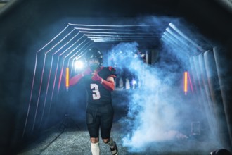 American football player in uniform and helmet emerging from a stadium tunnel filled with smoke and